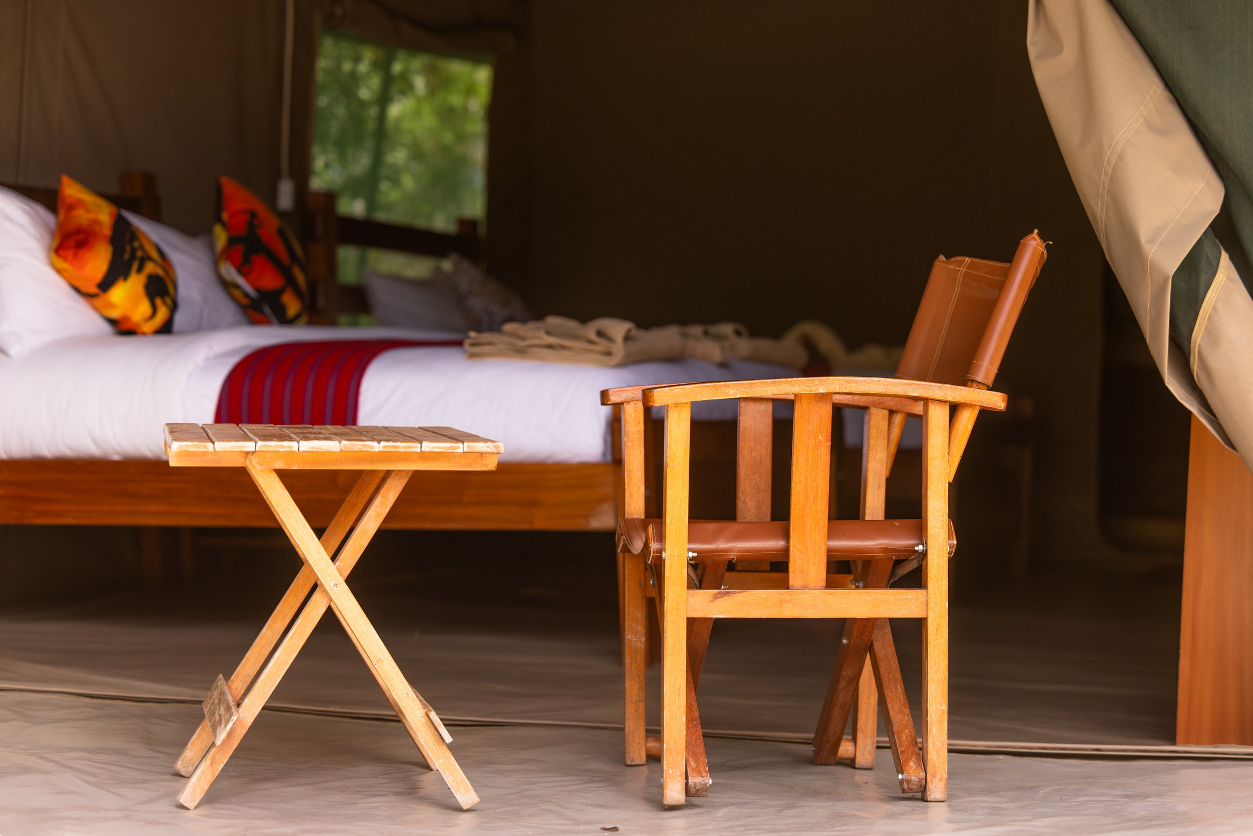 Safari tent interior with leather camp chair, wooden table and handcrafted bed