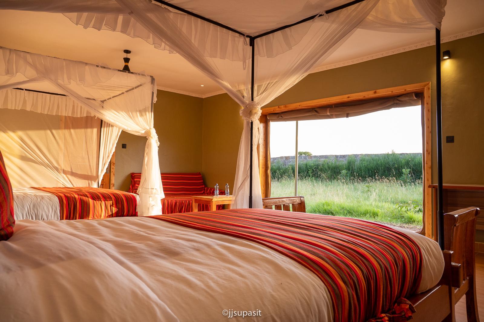 Four-poster canopy bed with open window framing the Mara grassland beyond